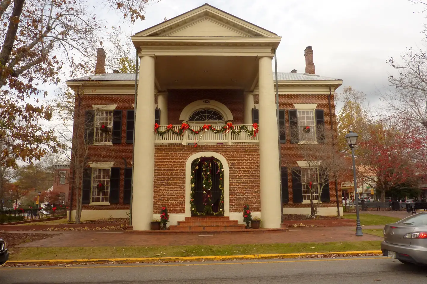 Front portico of the Dahlonega Gold Museum with garland on the balcony rail, a garland-framed arched doorway and wreaths in the windows.