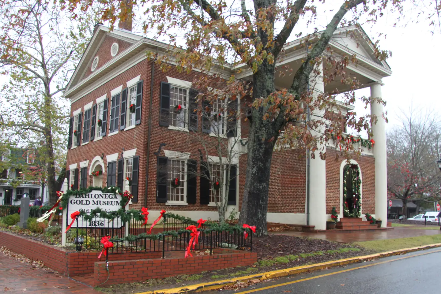 Red-brick Dahlonega Gold Museum with Christmas wreaths in the windows, garland on the fence and doorway, and its 1836 sign out front.