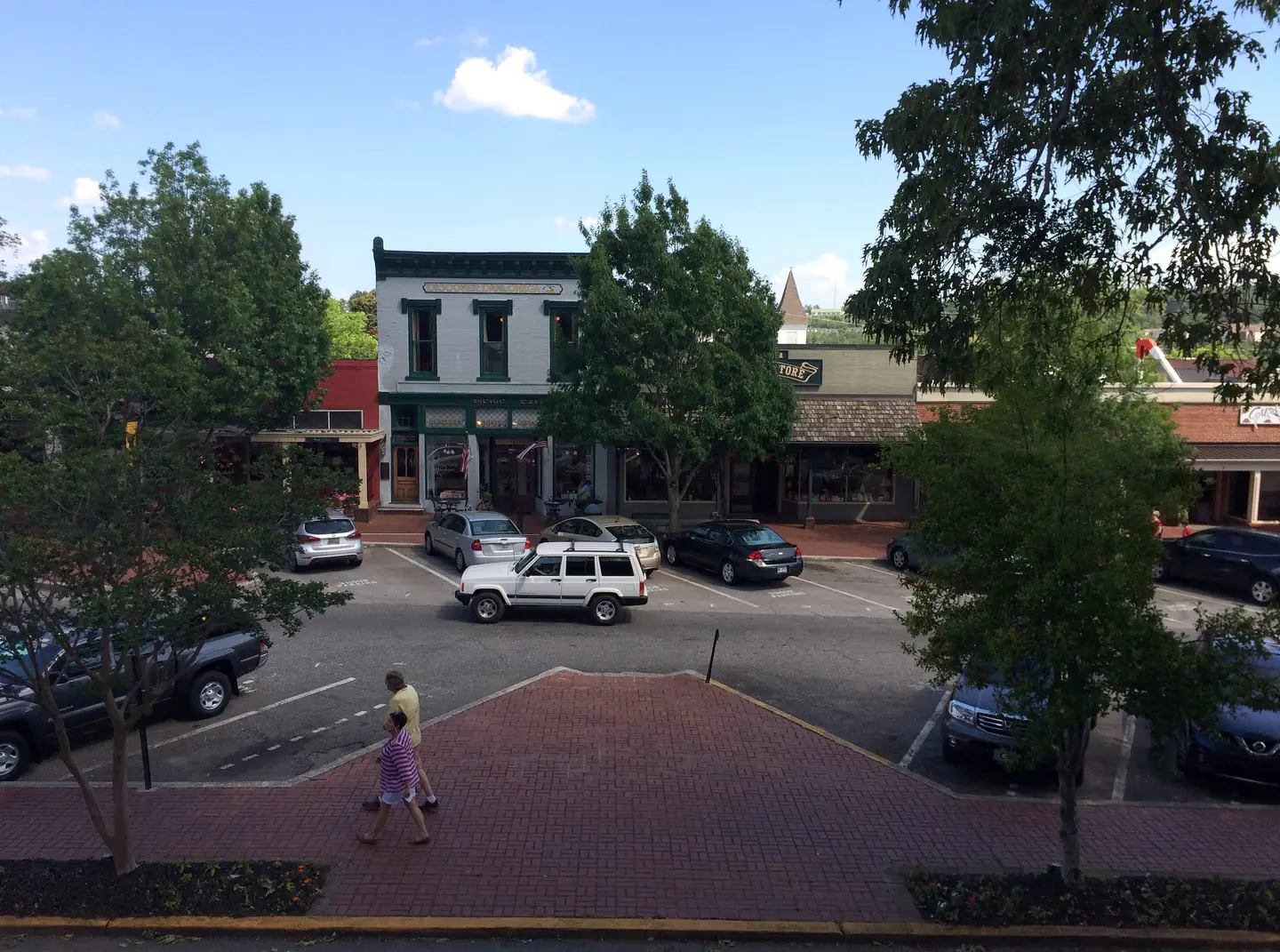 Elevated summer view of shops on Dahlonega's public square, with a white storefront signed 'Discover Dahlonega', parked cars and a brick plaza.
